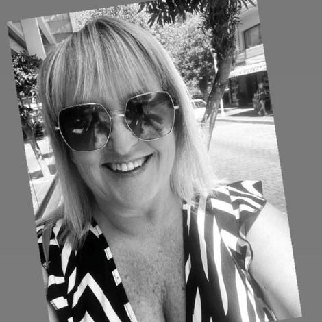 Smiling woman in sunglasses taking a selfie outdoors in a black-and-white patterned top