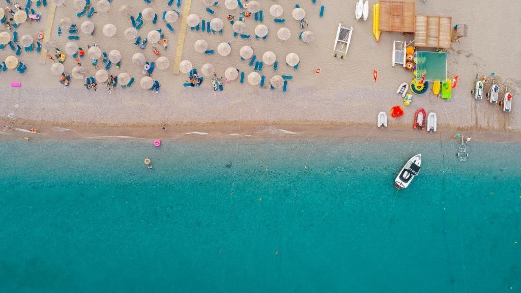 Aerial view of a crowded beach with rows of umbrellas, turquoise water, and a small boat near shore