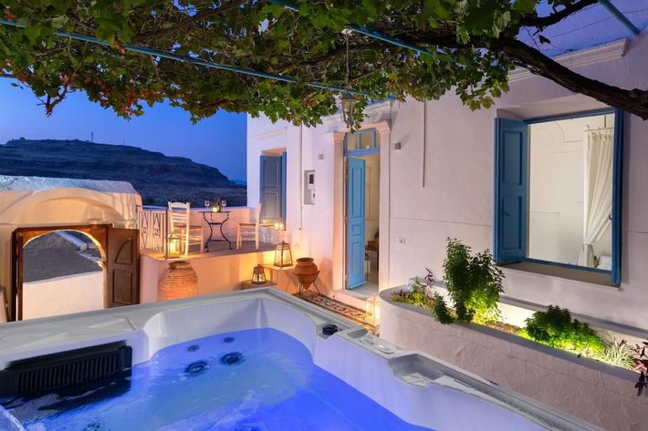White villa patio with lit hot tub, blue windows, and a vine-covered pergola at dusk