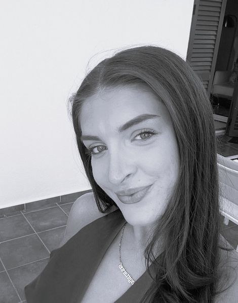 Close-up black-and-white selfie of a smiling person indoors, with a tiled floor and doorway in the background