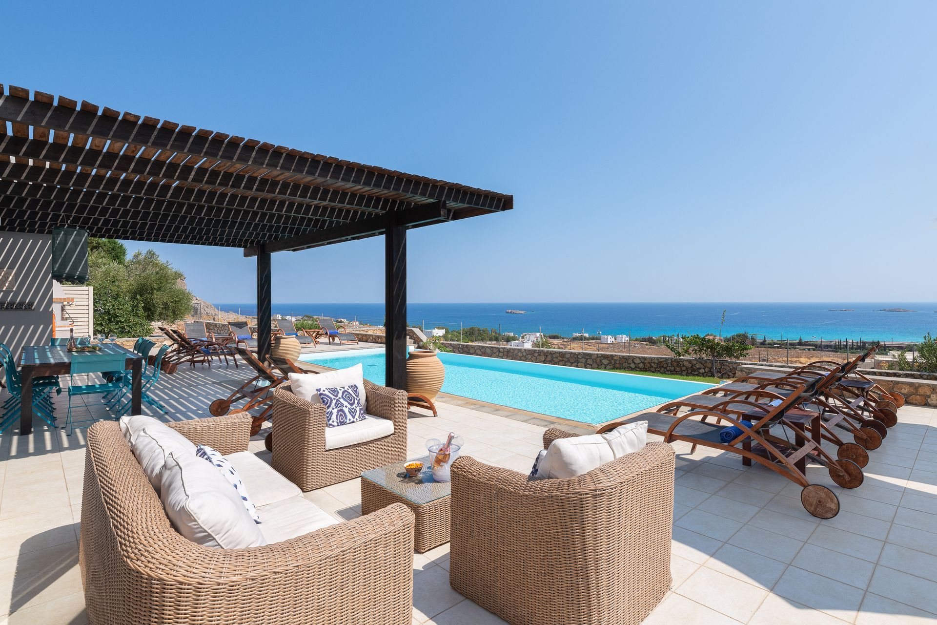 Resort terrace with wicker chairs and sun loungers beside a pool overlooking the ocean