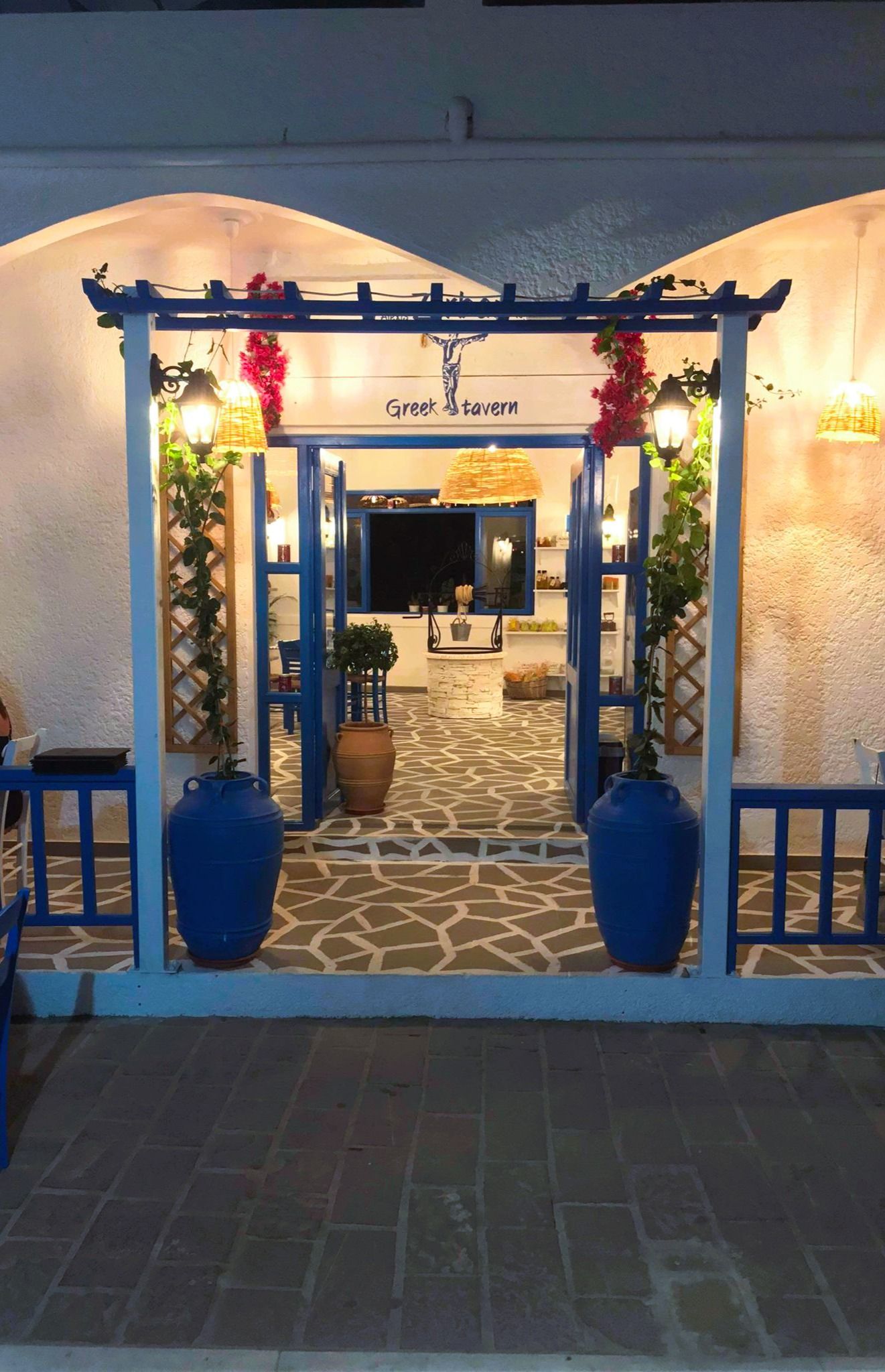 Blue-framed entrance with white walls, hanging flowers, and a stone-pattern walkway at dusk