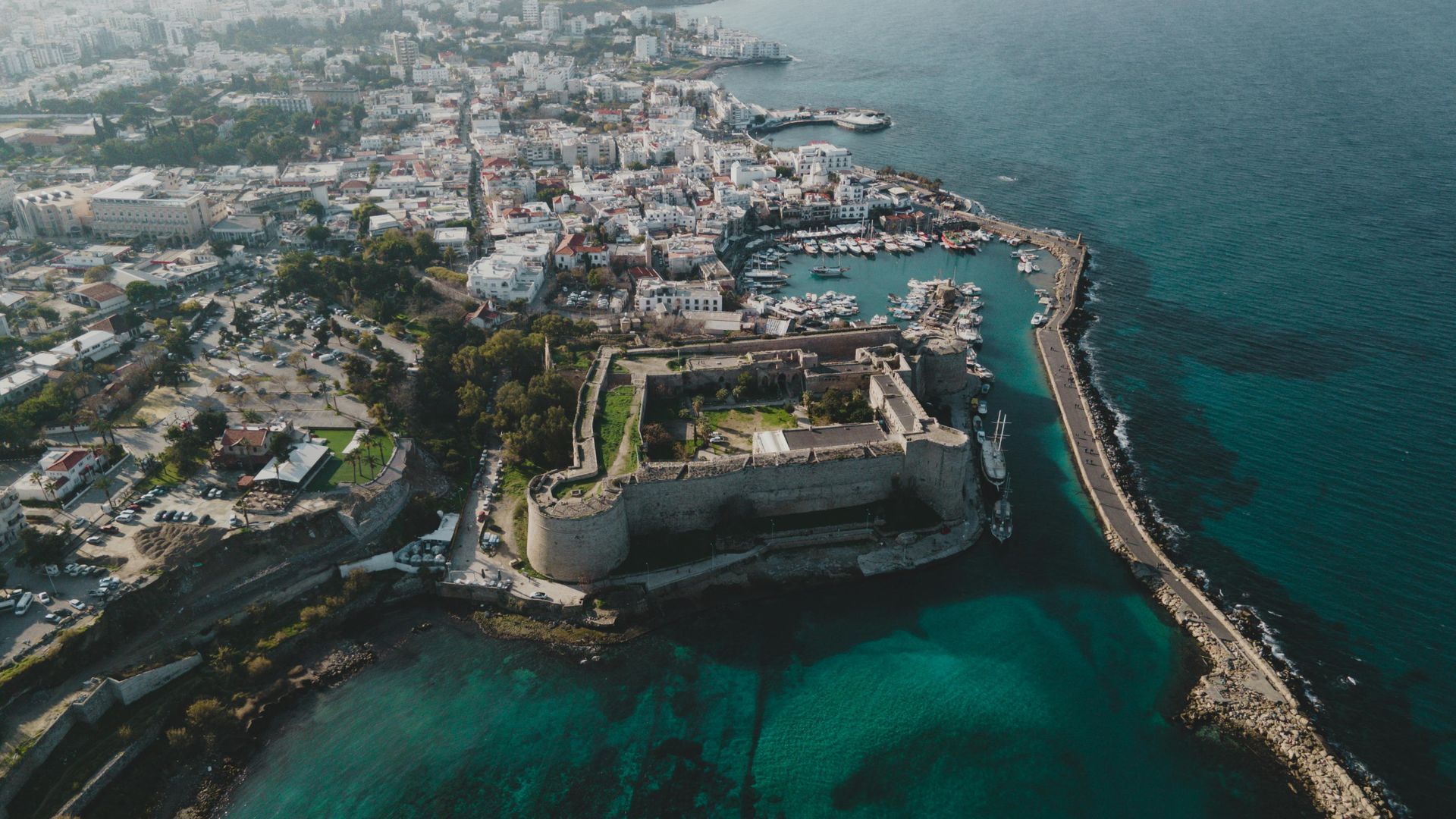 Aerial view of a coastal city with a historic fort, harbor, and turquoise ocean along the shoreline