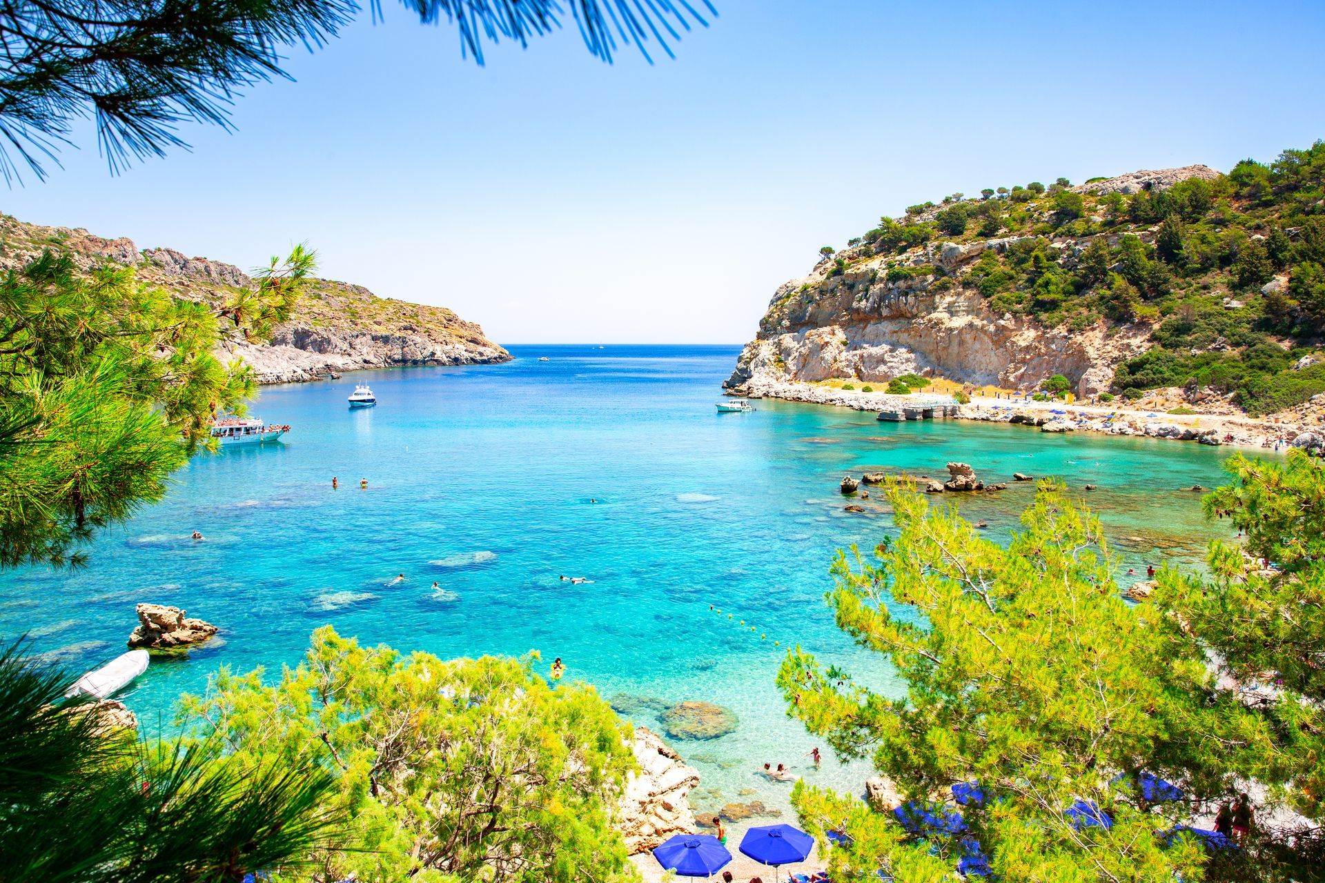 Turquoise cove with rocky cliffs, green shrubs, and calm blue sea under a clear sky