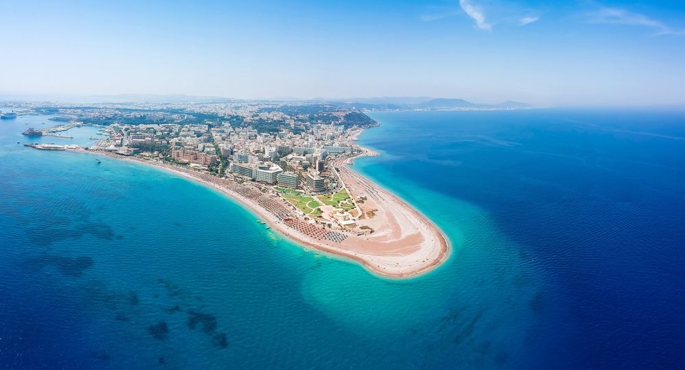 Aerial view of a coastal city on a narrow sandy peninsula surrounded by bright blue ocean.