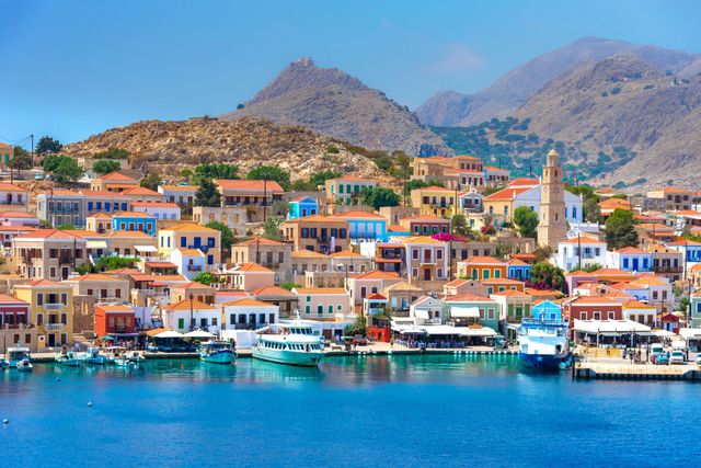 Colorful seaside village with boats, turquoise water, and mountains in the background