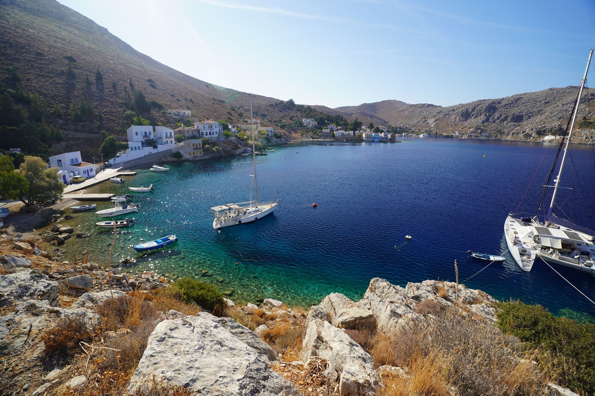 Aerial view of a rocky coastline with turquoise water, sandy beach, and white buildings near the shore