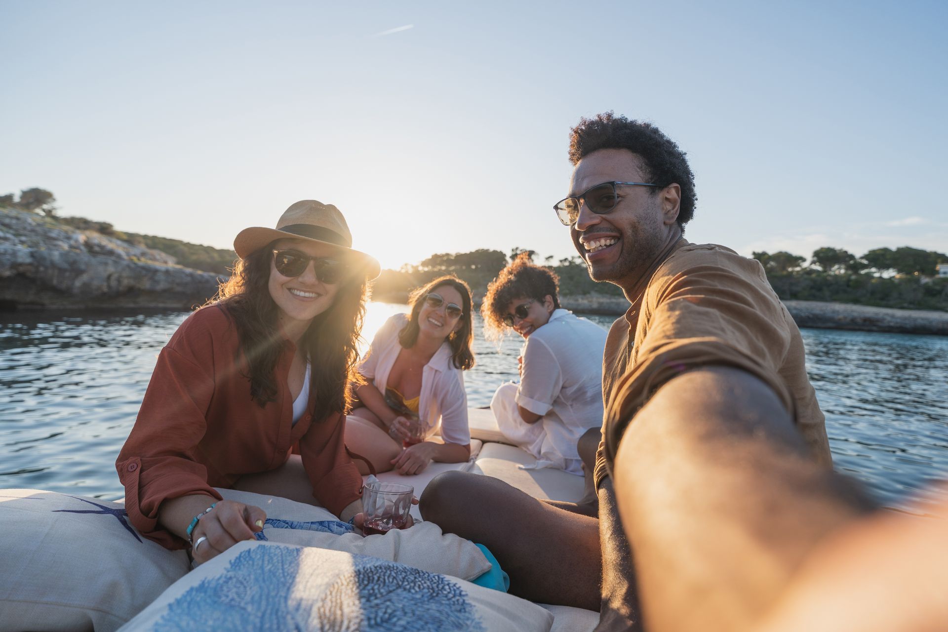 Friends sitting on a boat at sunset, smiling and taking a selfie on the water.
