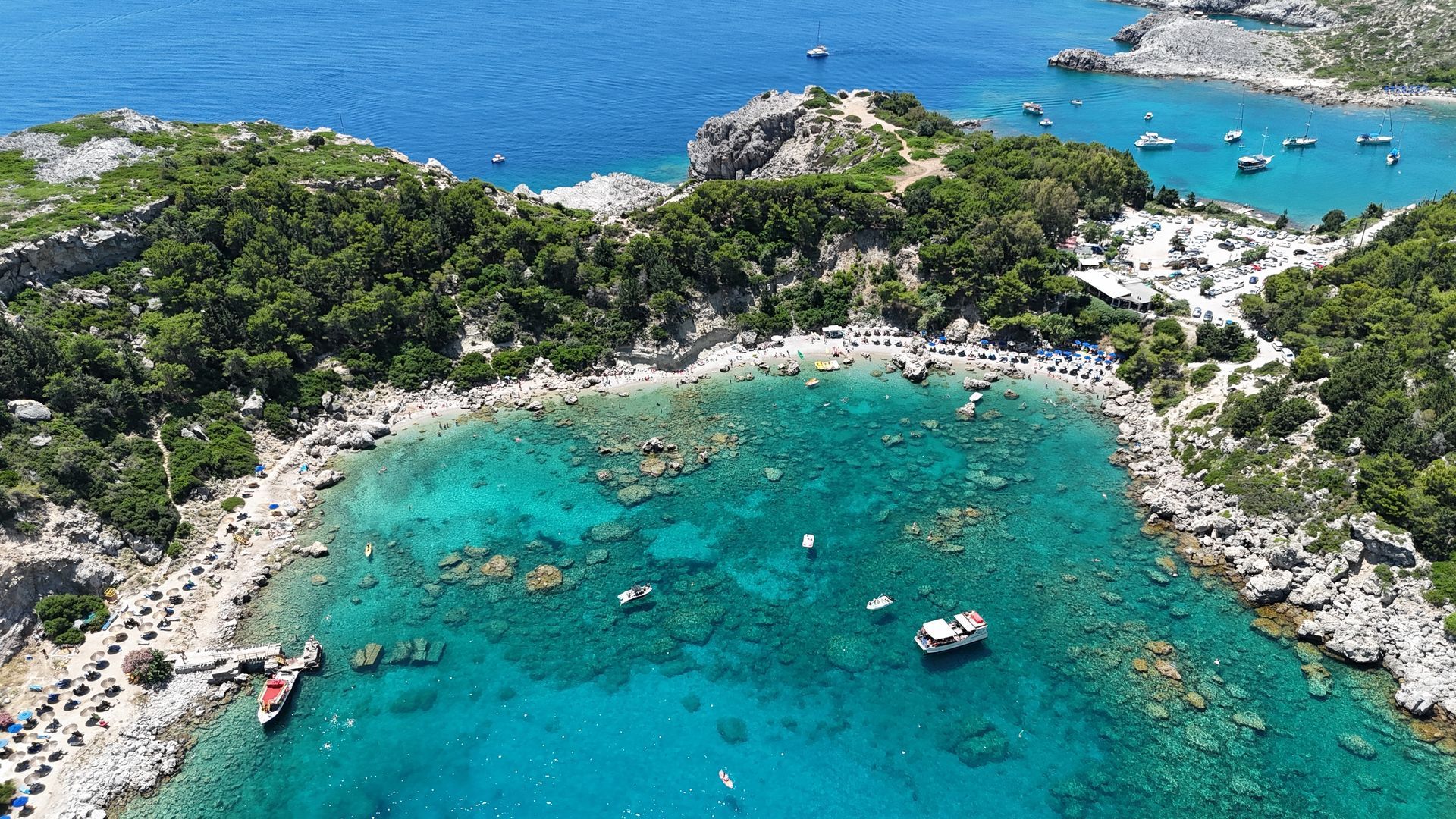 Aerial view of a turquoise cove with boats, rocky shoreline, and dense green vegetation
