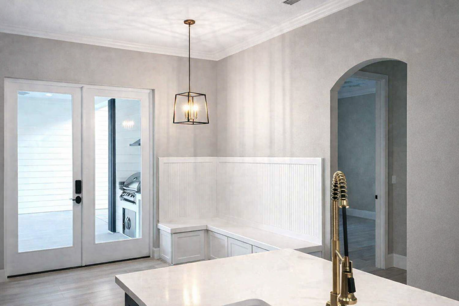 Bright dining nook with white wainscoting, pendant light, French doors, and a kitchen island edge in foreground