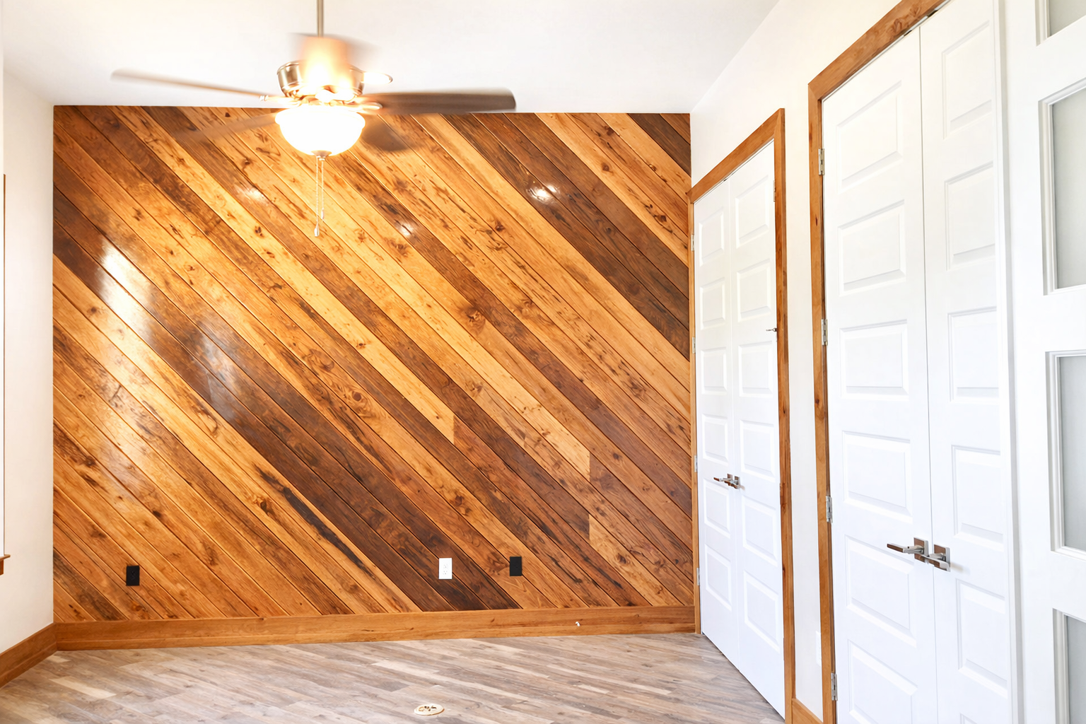 Empty room with diagonal wood accent wall, white doors, ceiling fan, and light gray floor
