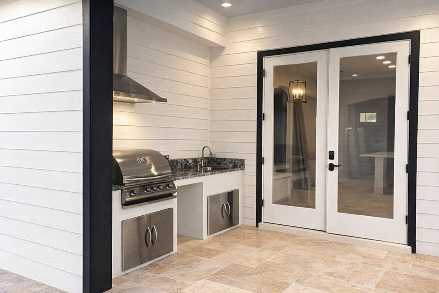 Modern outdoor kitchen with stainless grill, white shiplap walls, and French doors onto a patio