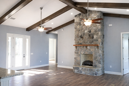 Spacious living room with vaulted ceiling, stone fireplace, ceiling fans, and gray walls with wood flooring