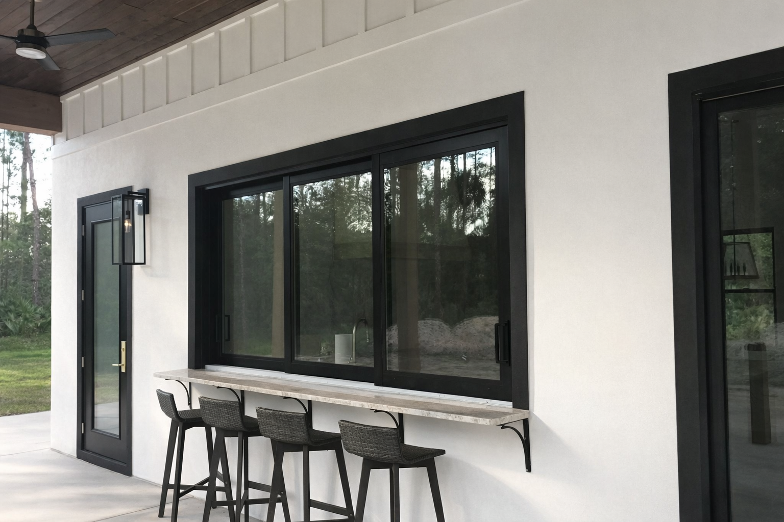 Modern patio with black-framed windows, white wall, and bar stools along a built-in counter.