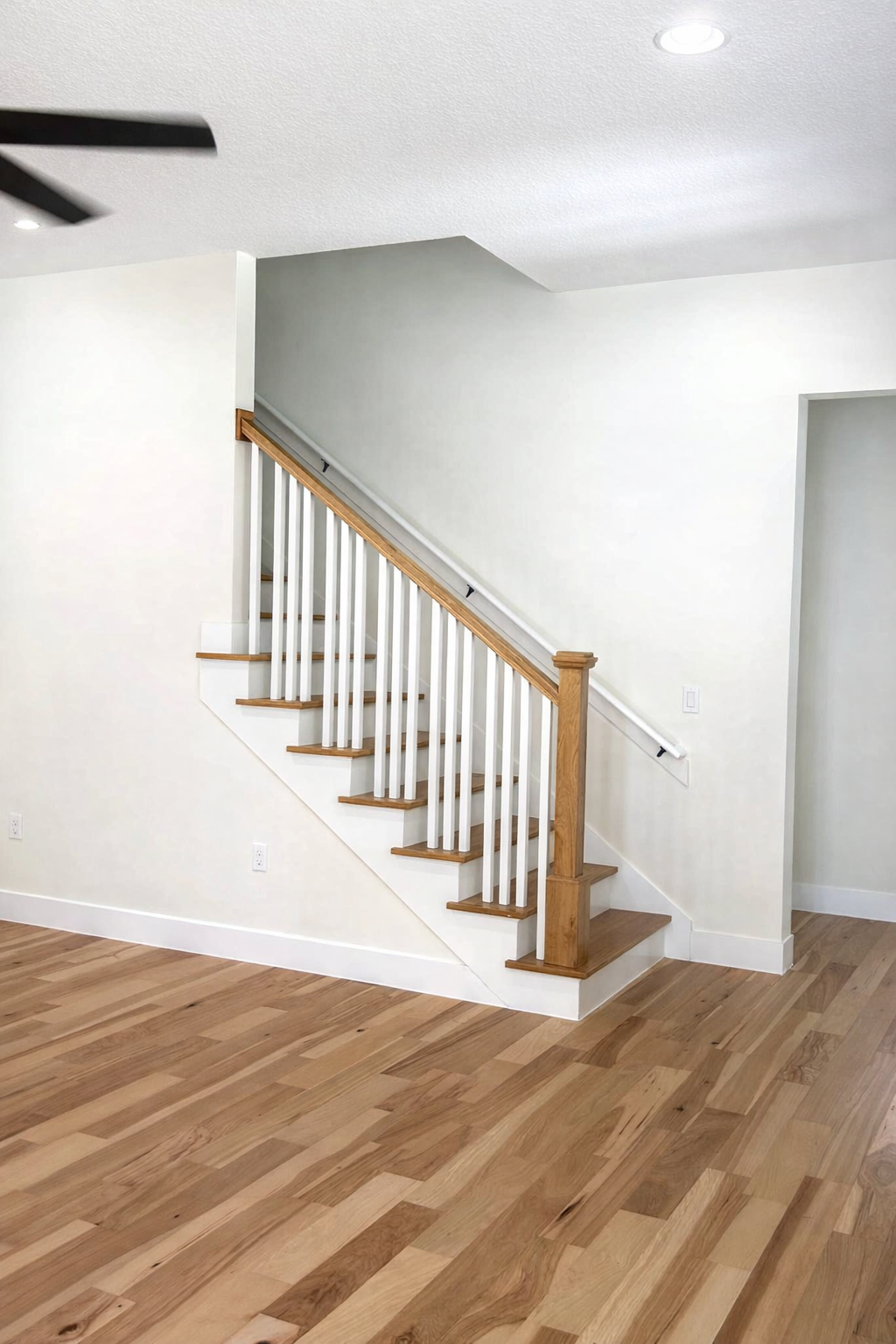 Empty room with hardwood floor and staircase with white walls and wooden handrail