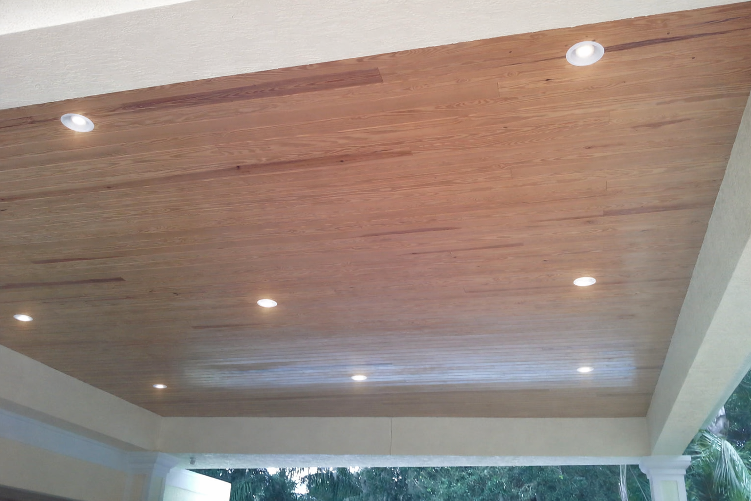 Wood-paneled ceiling with recessed lights on a covered outdoor patio