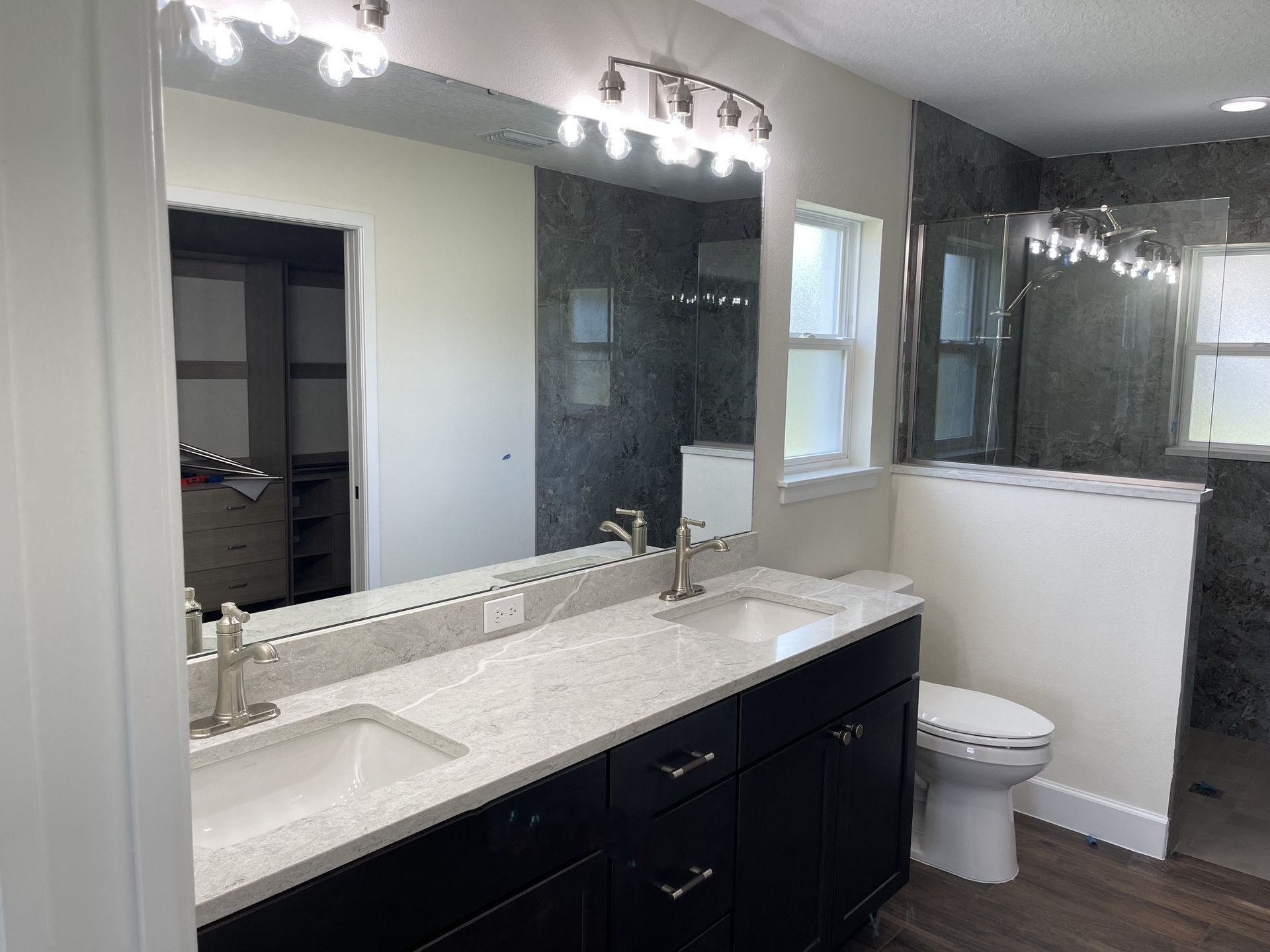 Modern bathroom with double vanity, large mirrors, and a toilet beside a glass shower.