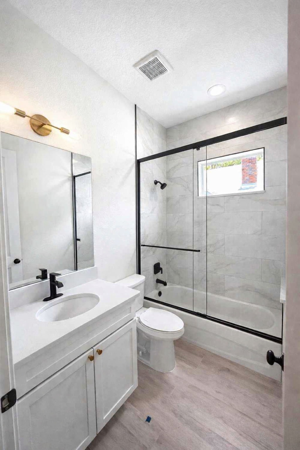 Modern bathroom with white vanity, mirror, and glass walk-in shower with black trim.