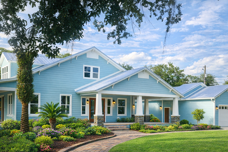 Light blue house with white trim, a covered porch, and a landscaped front yard under a bright sky