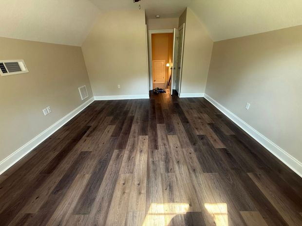 Empty room with dark wood floors, beige walls, and sunlight near an open doorway.