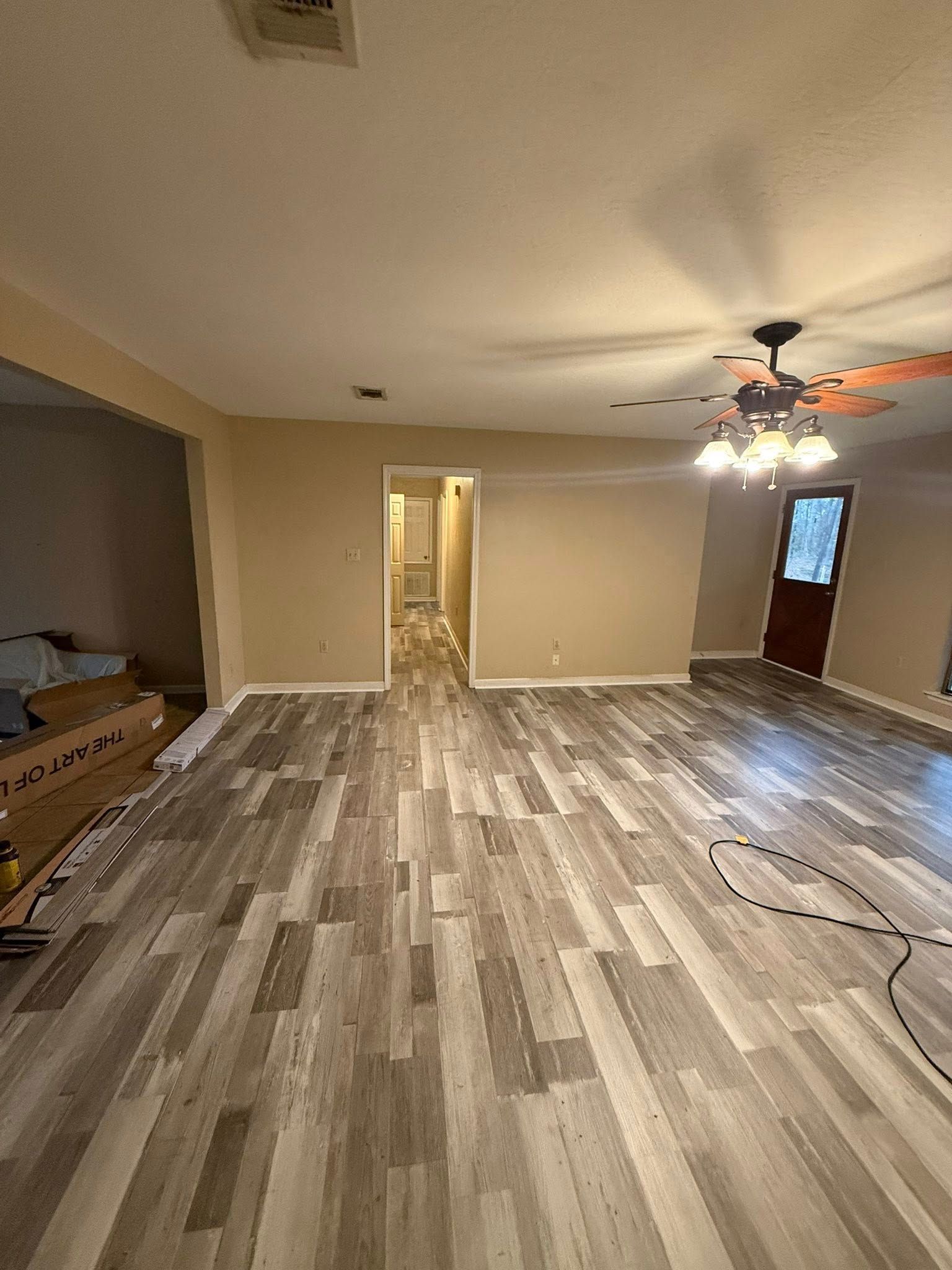 Empty living room with wood-look flooring, beige walls, ceiling fan, and a front door.