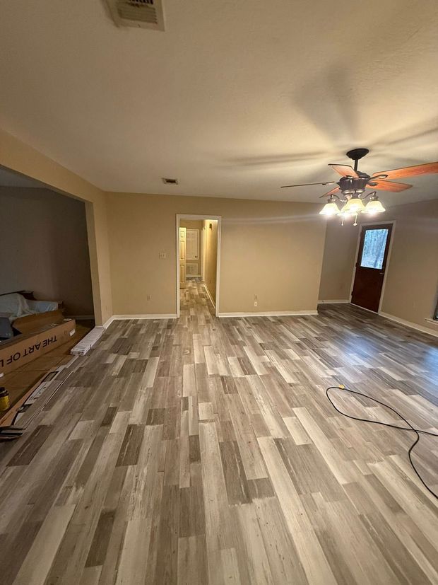 Empty living room with wood-look flooring, beige walls, ceiling fan, and a front door.