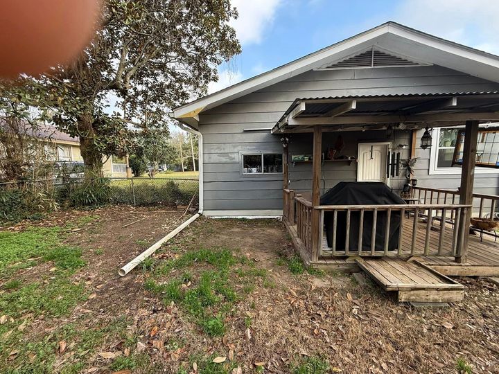 Small gray house with a covered porch and railing, viewed from the yard with leaves scattered on the ground
