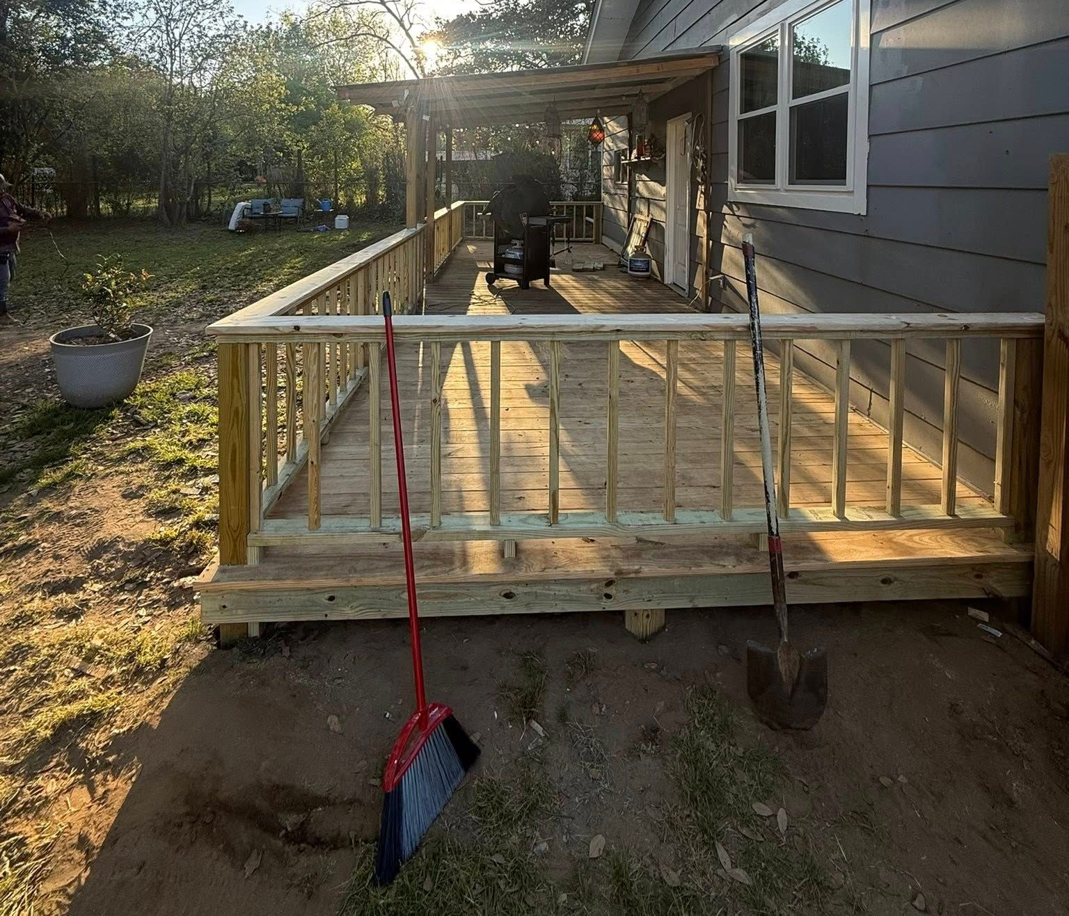 Wooden porch deck beside a gray house, with a red broom leaning against the railing.