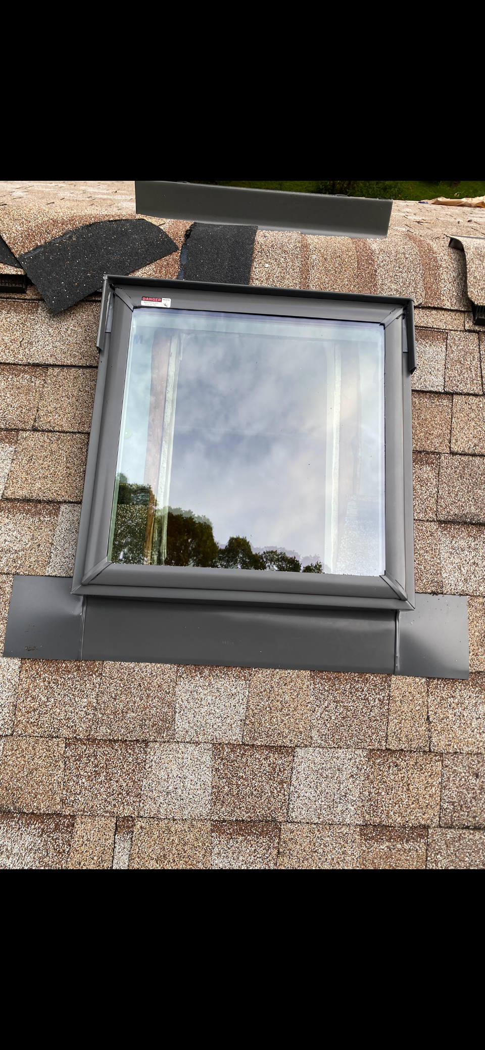 A skylight installed on a shingled roof with dark grey metal flashing visible around its frame.