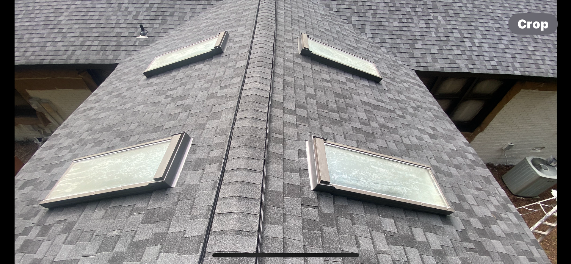 An overhead view of a gray shingled roof featuring four skylights symmetrically arranged on two slanted sides.