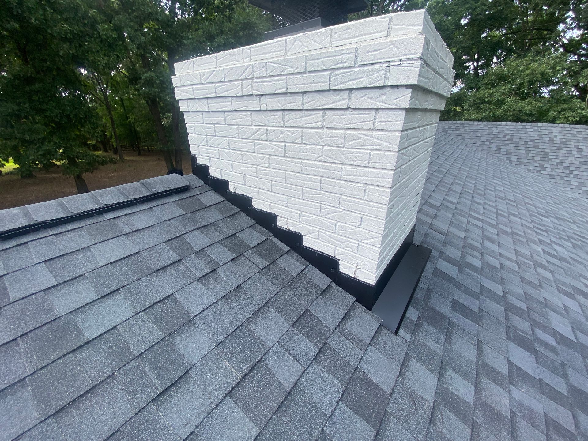 A white brick chimney on a shingled residential roof with black flashing installed at the base.