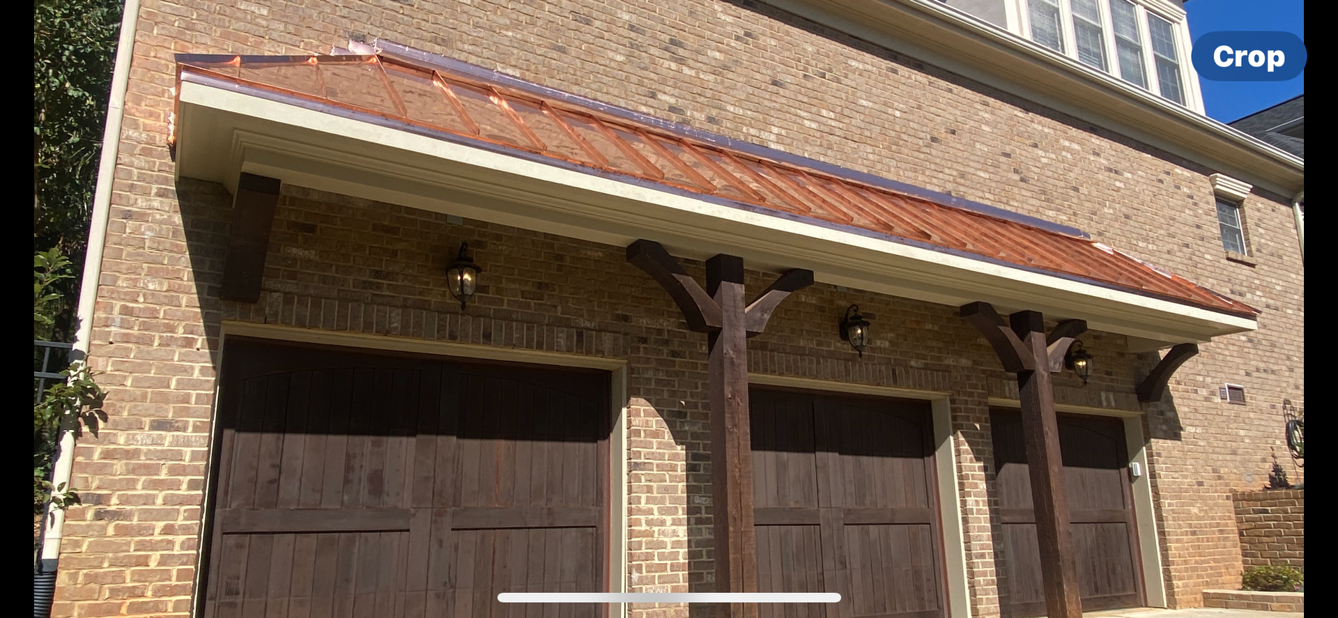 Brick garage exterior with three dark doors, wooden support beams, and a sloped copper-colored metal roof.