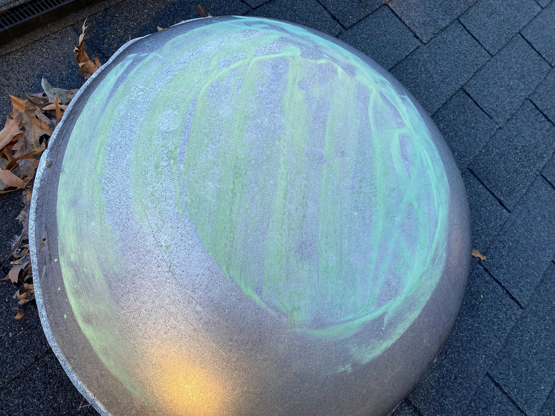 A large, textured concrete sphere on a paved surface, featuring a swirl of faded green chalk drawing on its top surface.