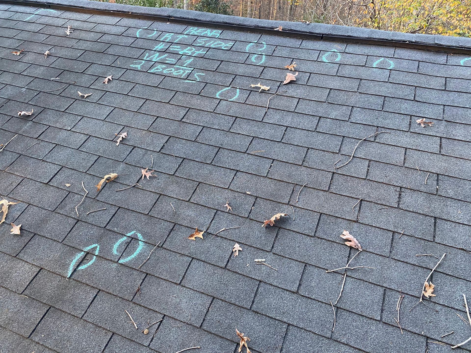 Gray asphalt roof shingles marked with light blue chalk circles and markings, likely identifying damage or repair needs.