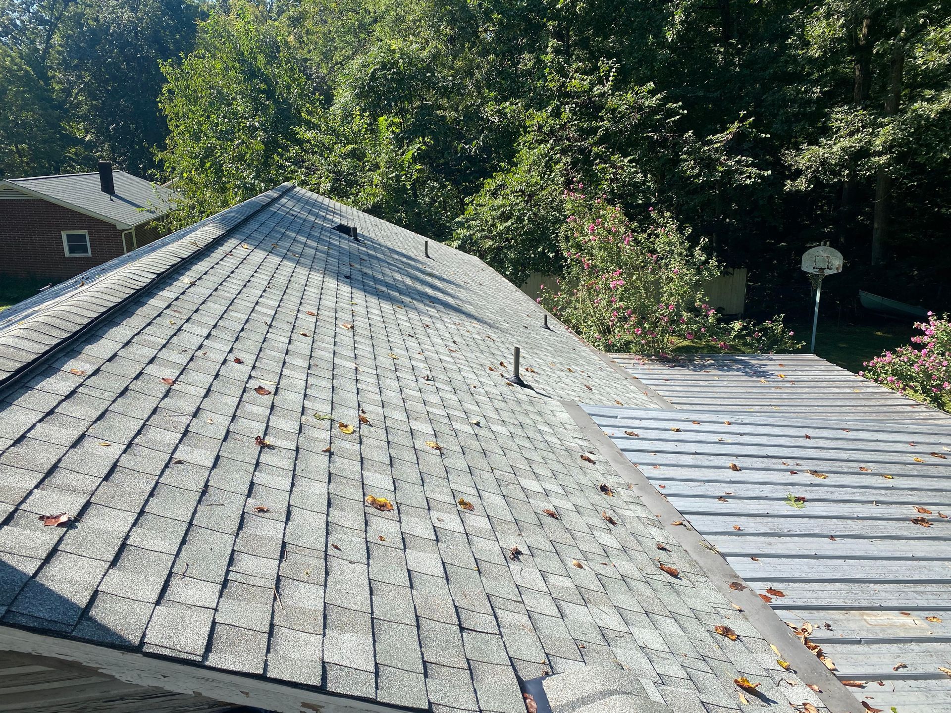 An angled, high-view of a grey asphalt shingled roof with a prominent ridge line and a metal pipe vent.