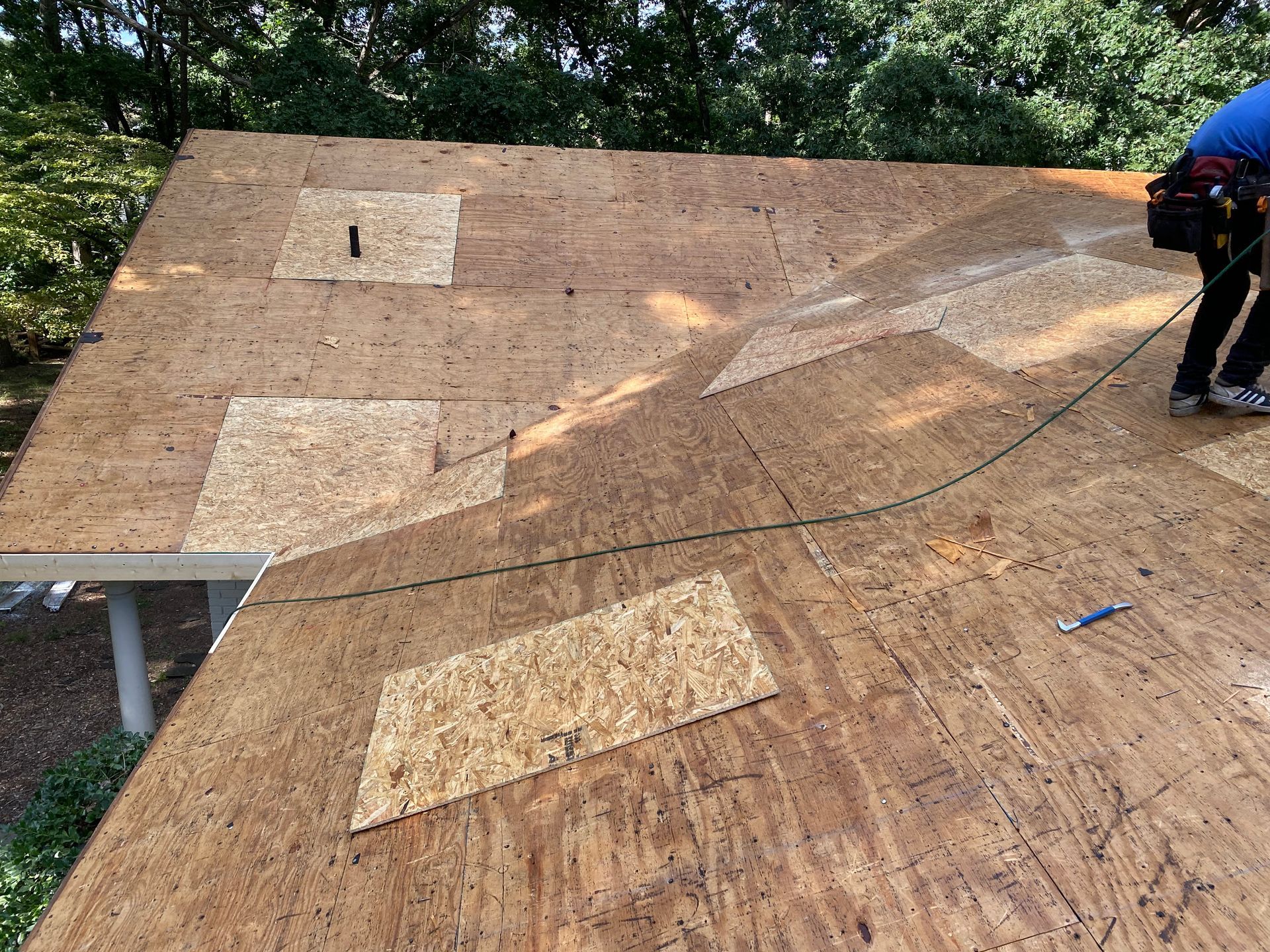 A worker standing on a wooden roof deck during a repair, with several new plywood patches installed on the surface.