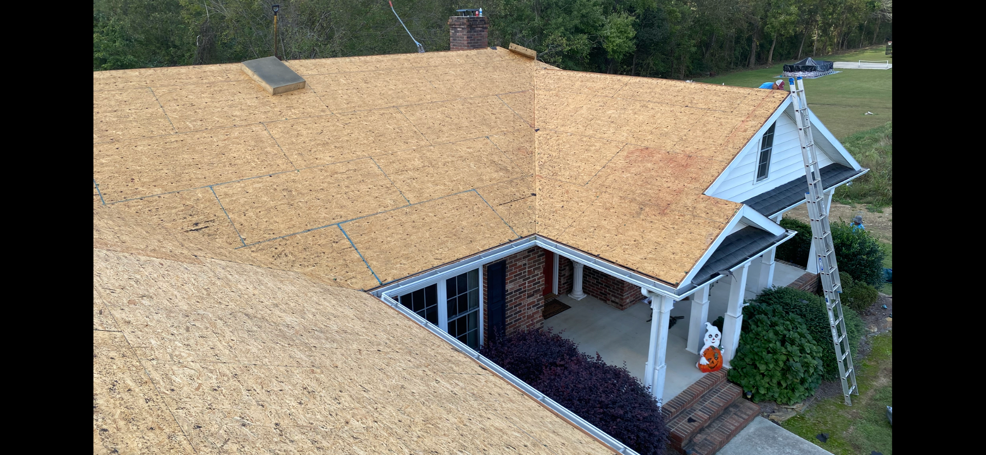 An elevated view of a house roof undergoing renovation with new plywood sheathing and a ladder resting against the eaves.
