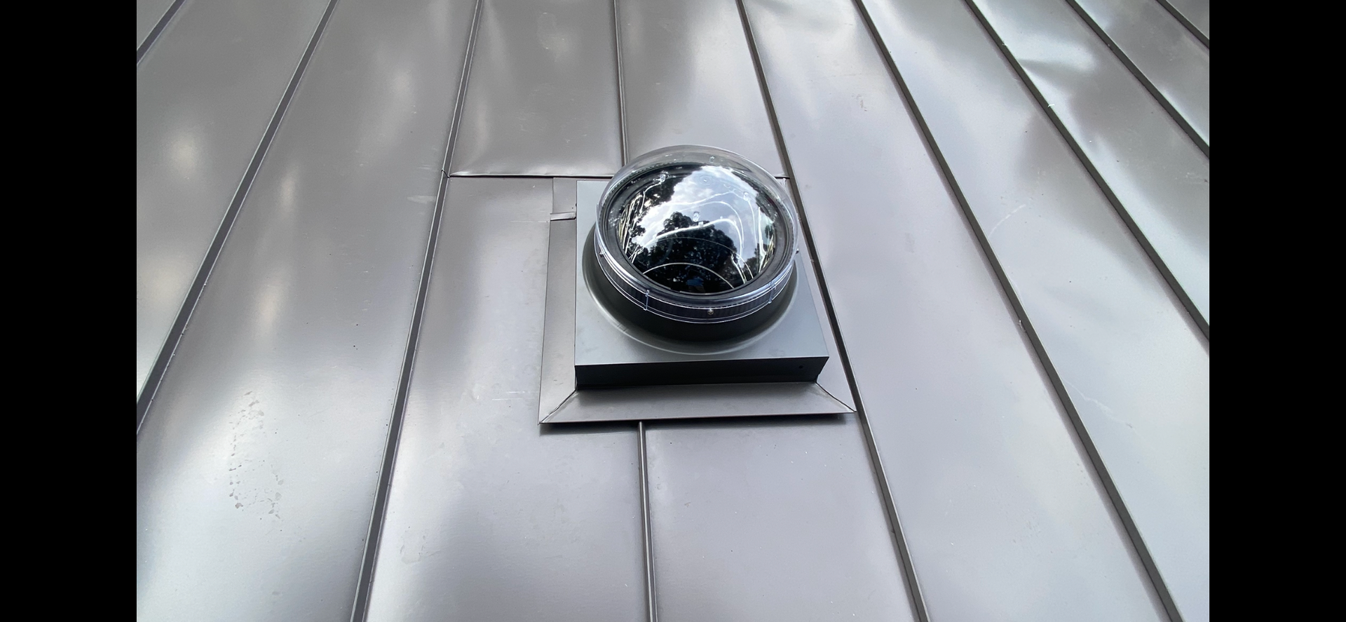 A damaged, cracked clear dome skylight mounted on a grey metal standing seam roof.