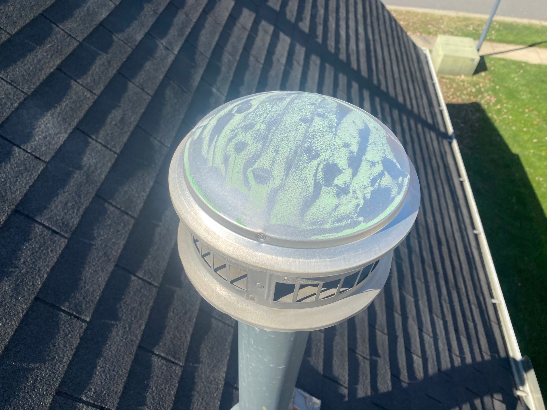 A white round chimney cap with a mossy, weathered dome sitting on a gray roof with dark asphalt shingles.
