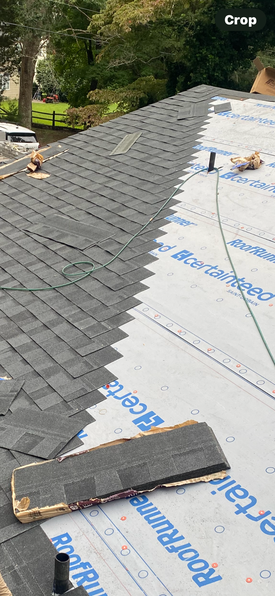A partially installed asphalt shingle roof with gray shingles over white synthetic underlayment on a sunny day.
