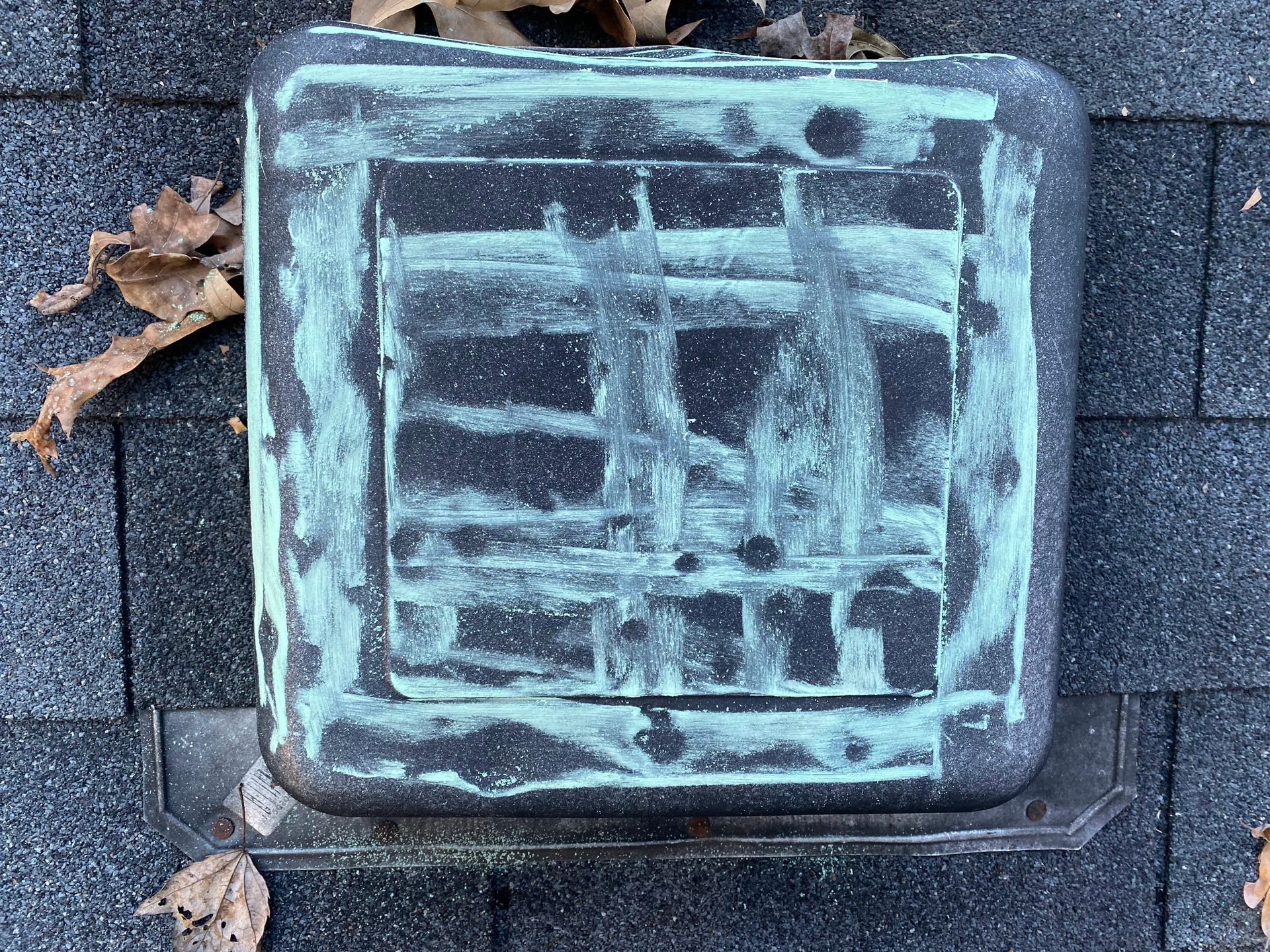 A black square roof vent with green streaks of weathered material, installed on dark grey asphalt shingles.