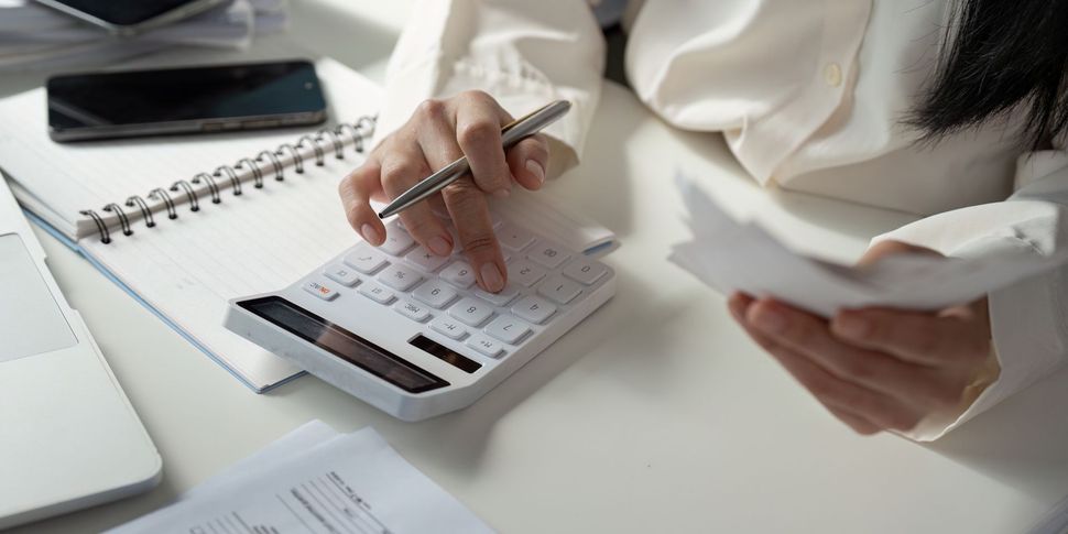 Person using a calculator while holding papers, possibly reviewing financial documents at a desk. Person using a calculator while holding papers, possibly reviewing financial documents at a desk.