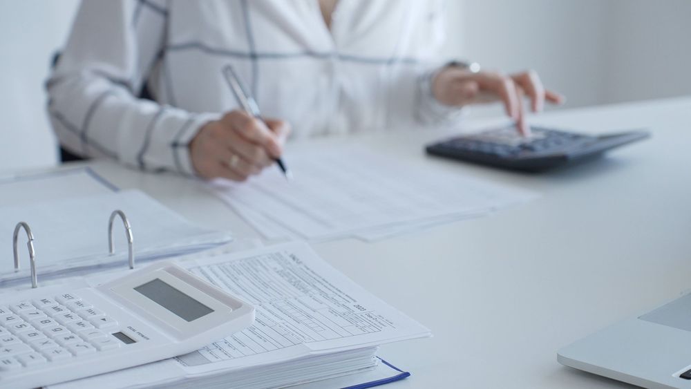 Woman using calculator and pen at a desk with paperwork and binder. Woman using calculator and pen at a desk with paperwork and binder.