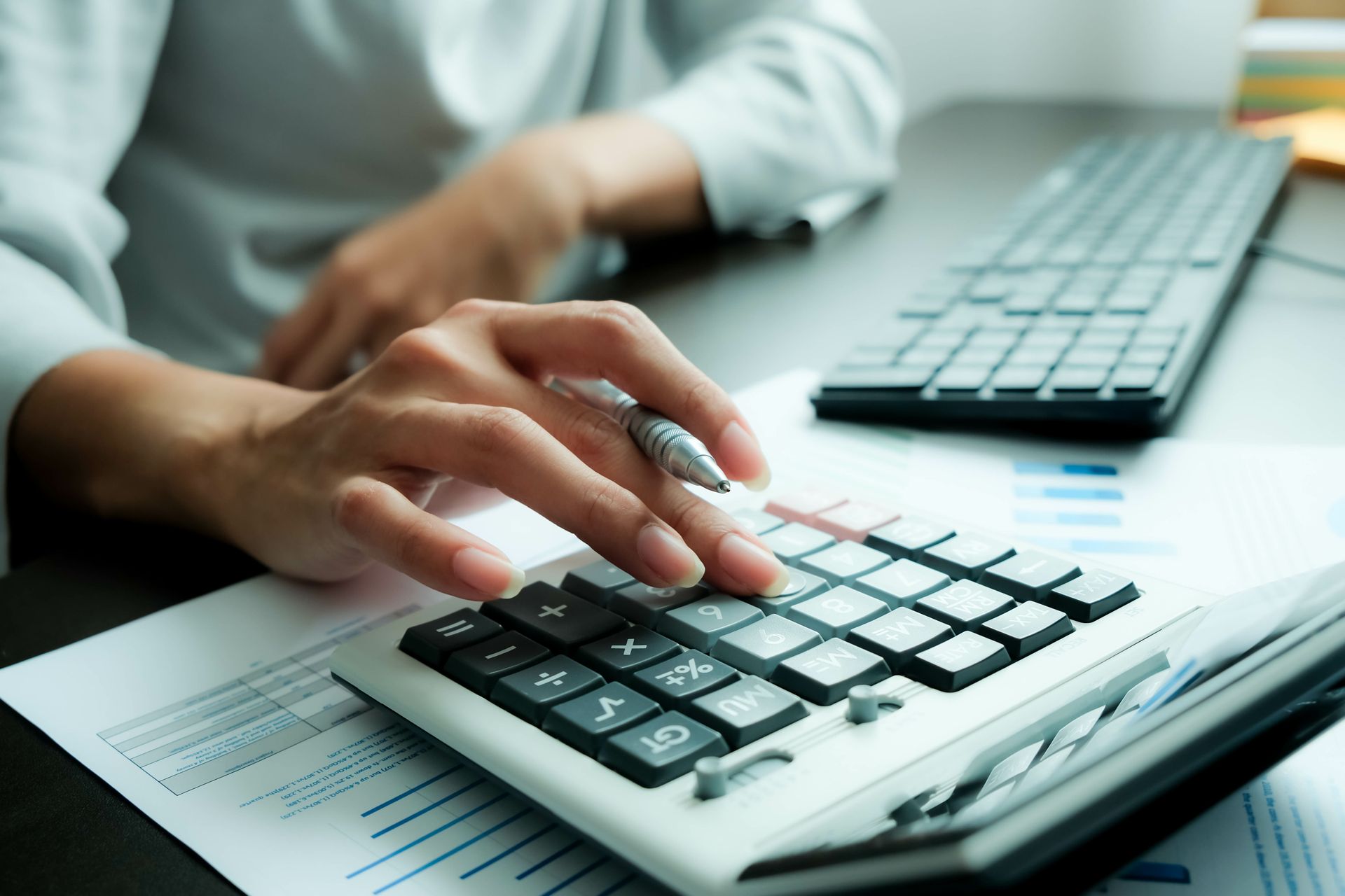 Person's hands using a calculator on a desk with papers and a keyboard. Person's hands using a calculator on a desk with papers and a keyboard.