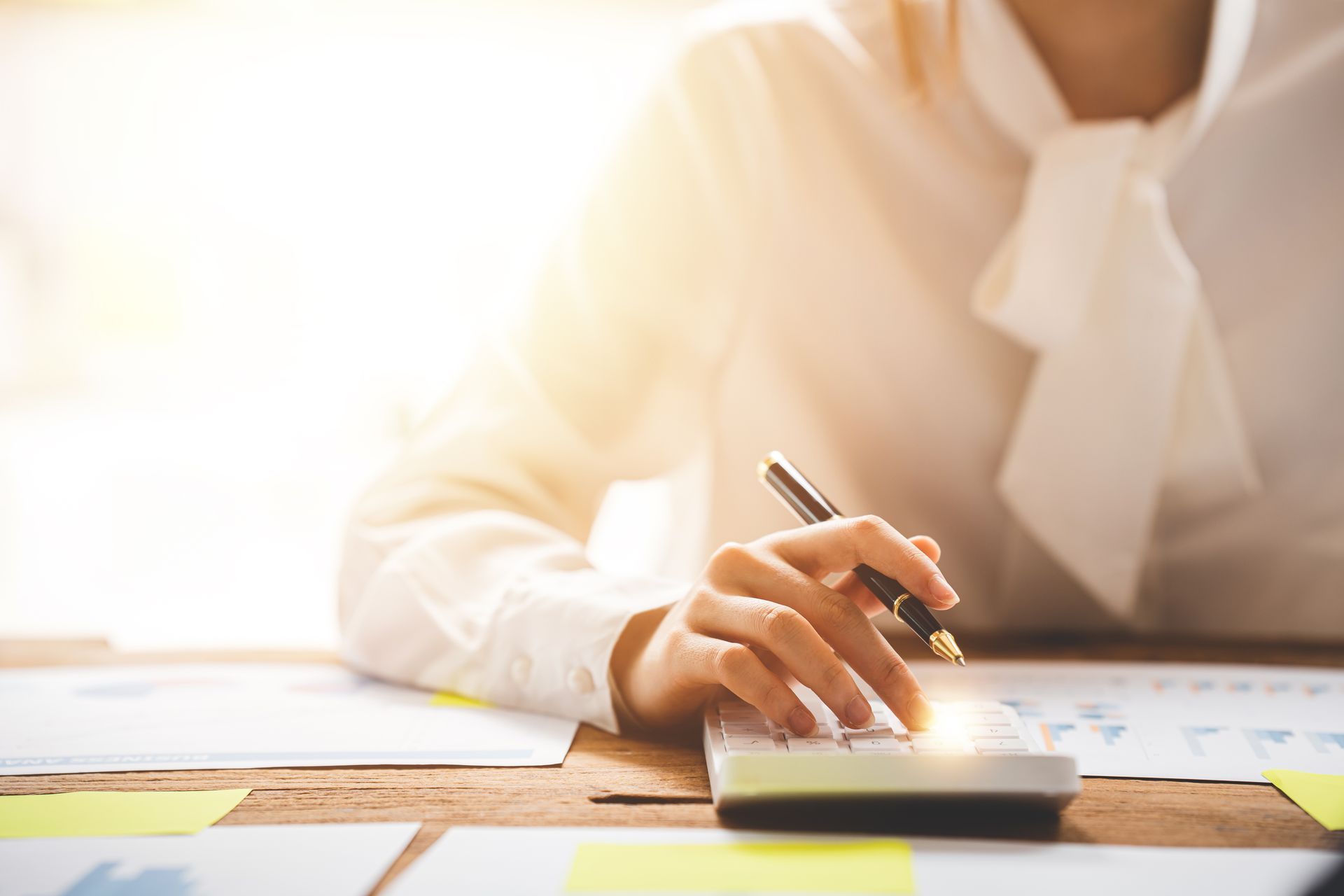 Woman in white blouse using a calculator with documents on a wooden desk. Woman in white blouse using a calculator with documents on a wooden desk.