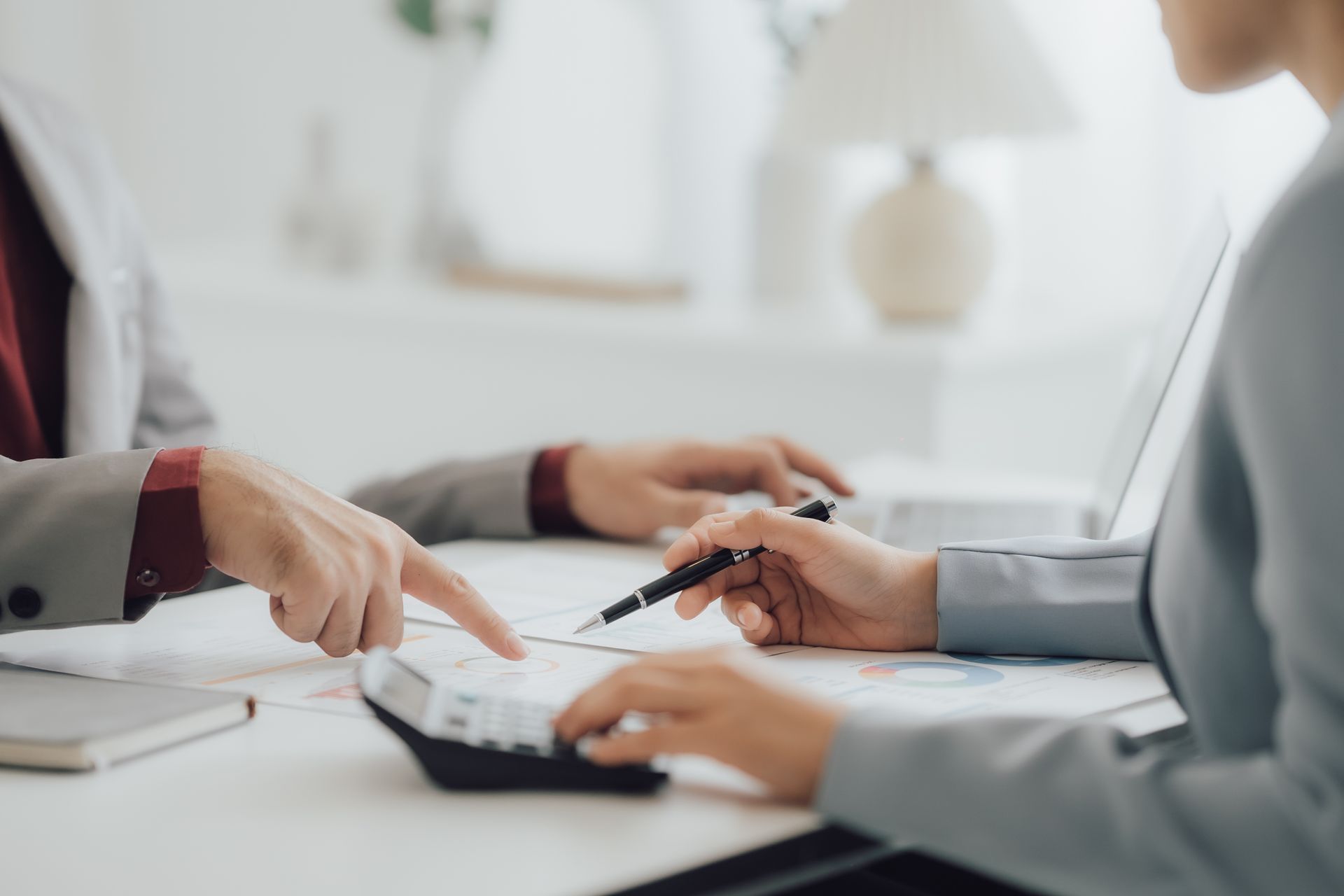 Two people reviewing financial documents, using a calculator, with hands pointing and gesturing. Two people reviewing financial documents, using a calculator, with hands pointing and gesturing.