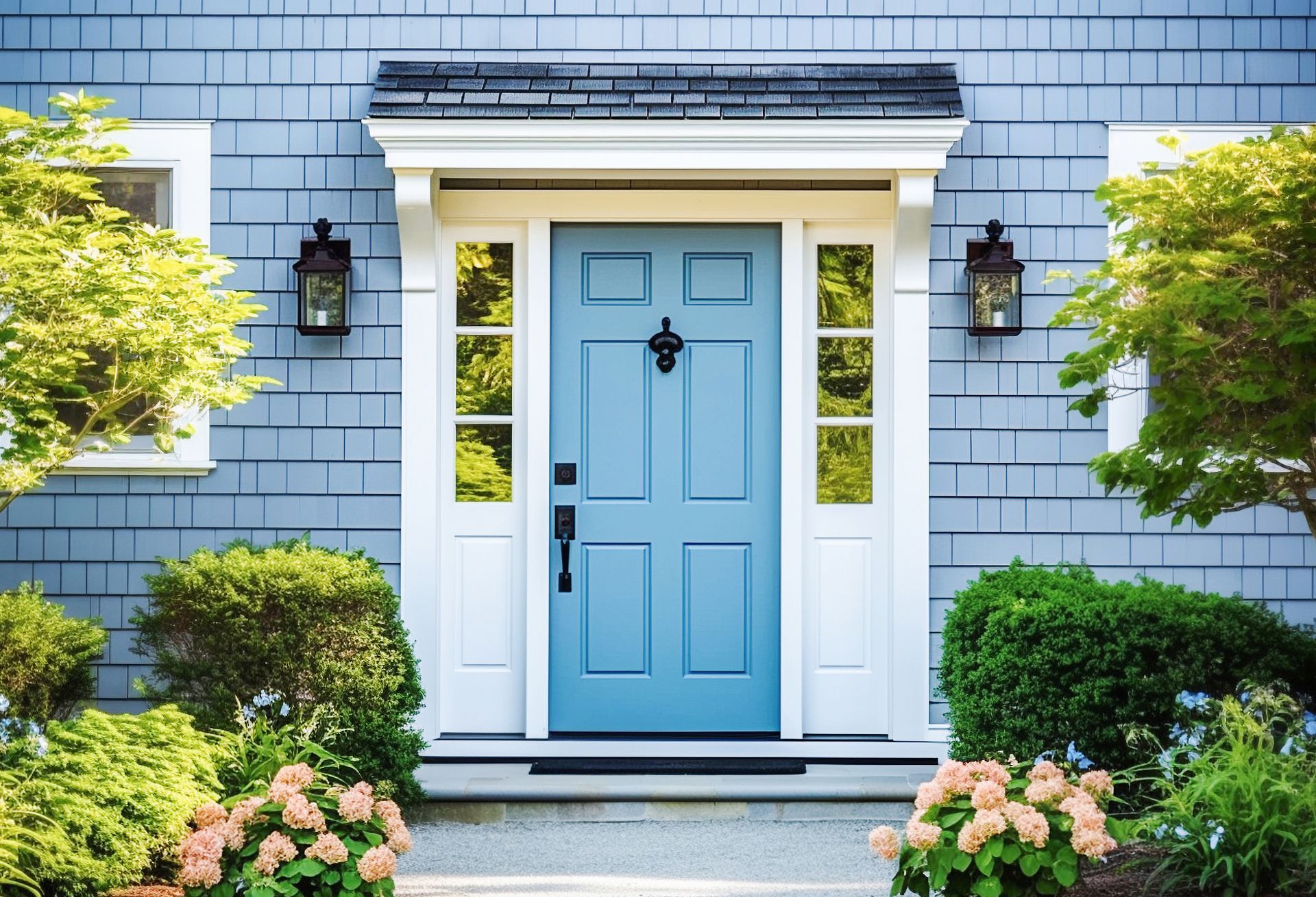 Light blue front door with white trim on a blue shingled house, framed by greenery and flowers