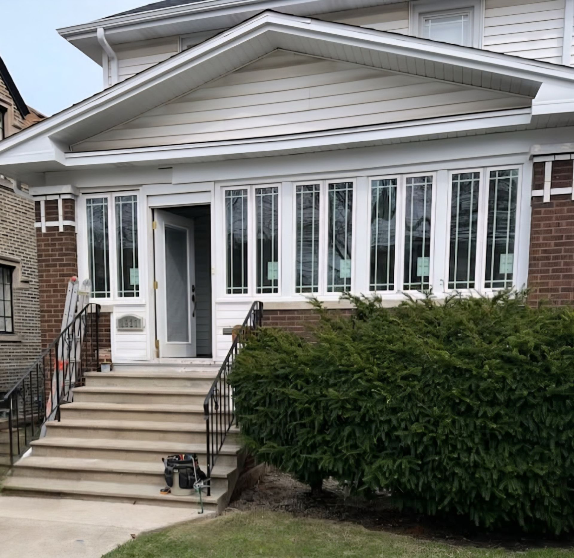 A house with a front porch, brick facade, stairs, and a partially open door.