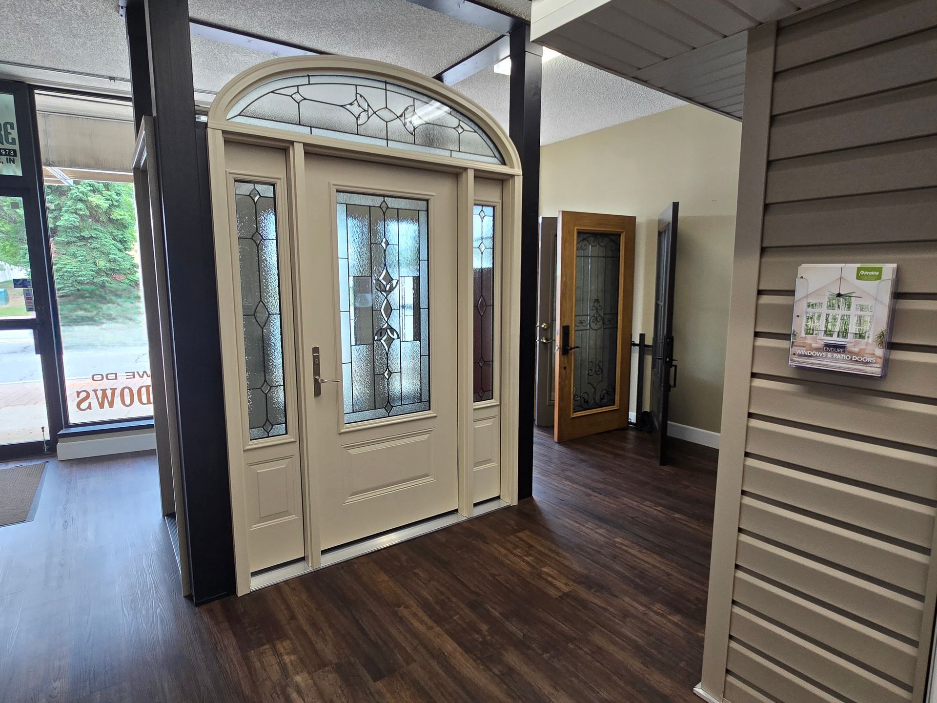 Door showroom with a display door, side panels, and arched top; brown floor and siding.
