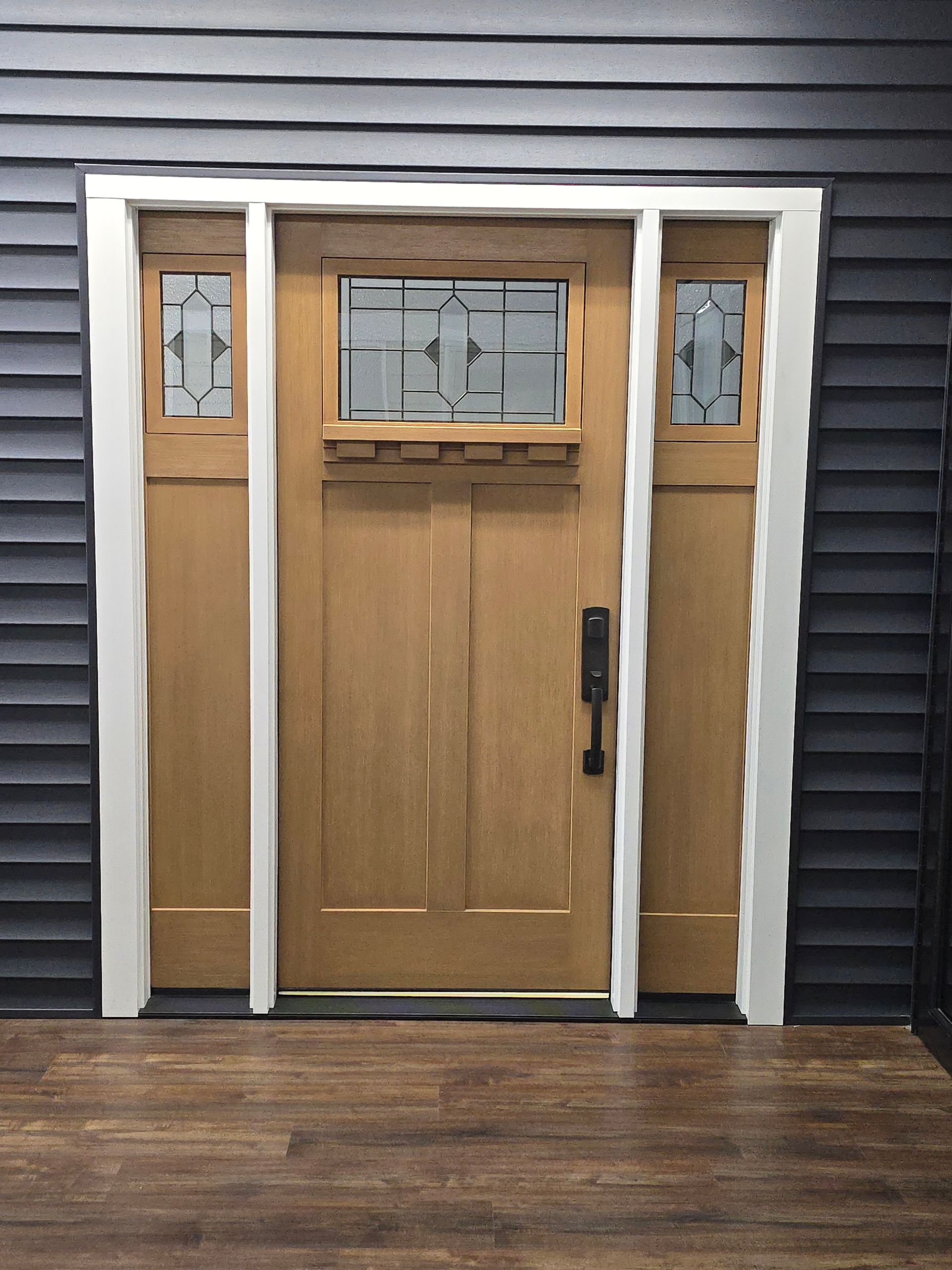 Wooden craftsman-style front door with glass panels, set in a white frame, against a dark blue-gray siding.